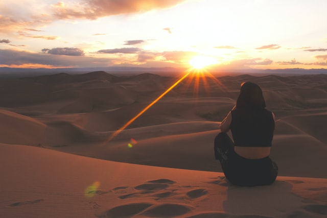 砂漠で夕日を眺める女性